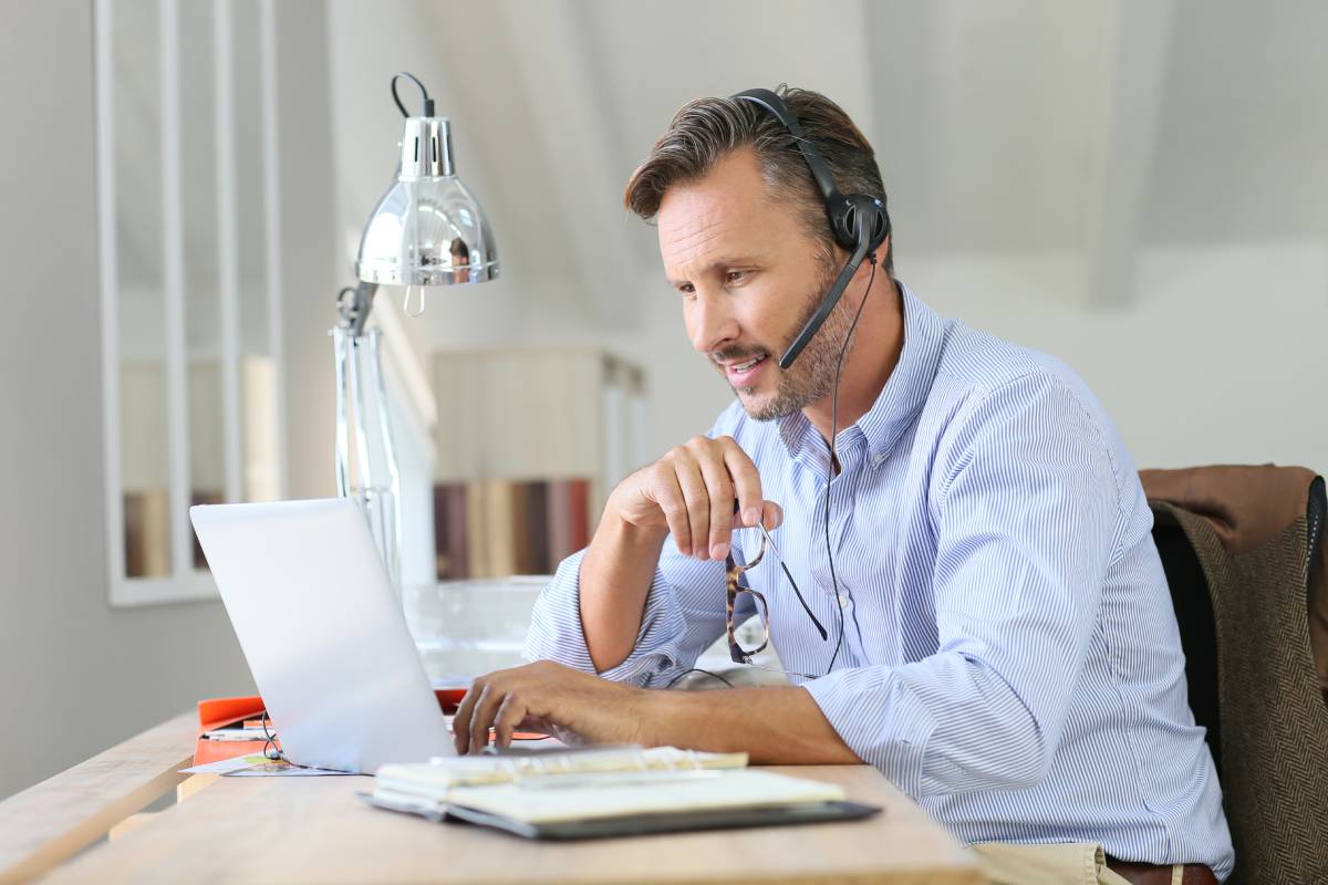 A man working from home at his desk using a laptop and a headset